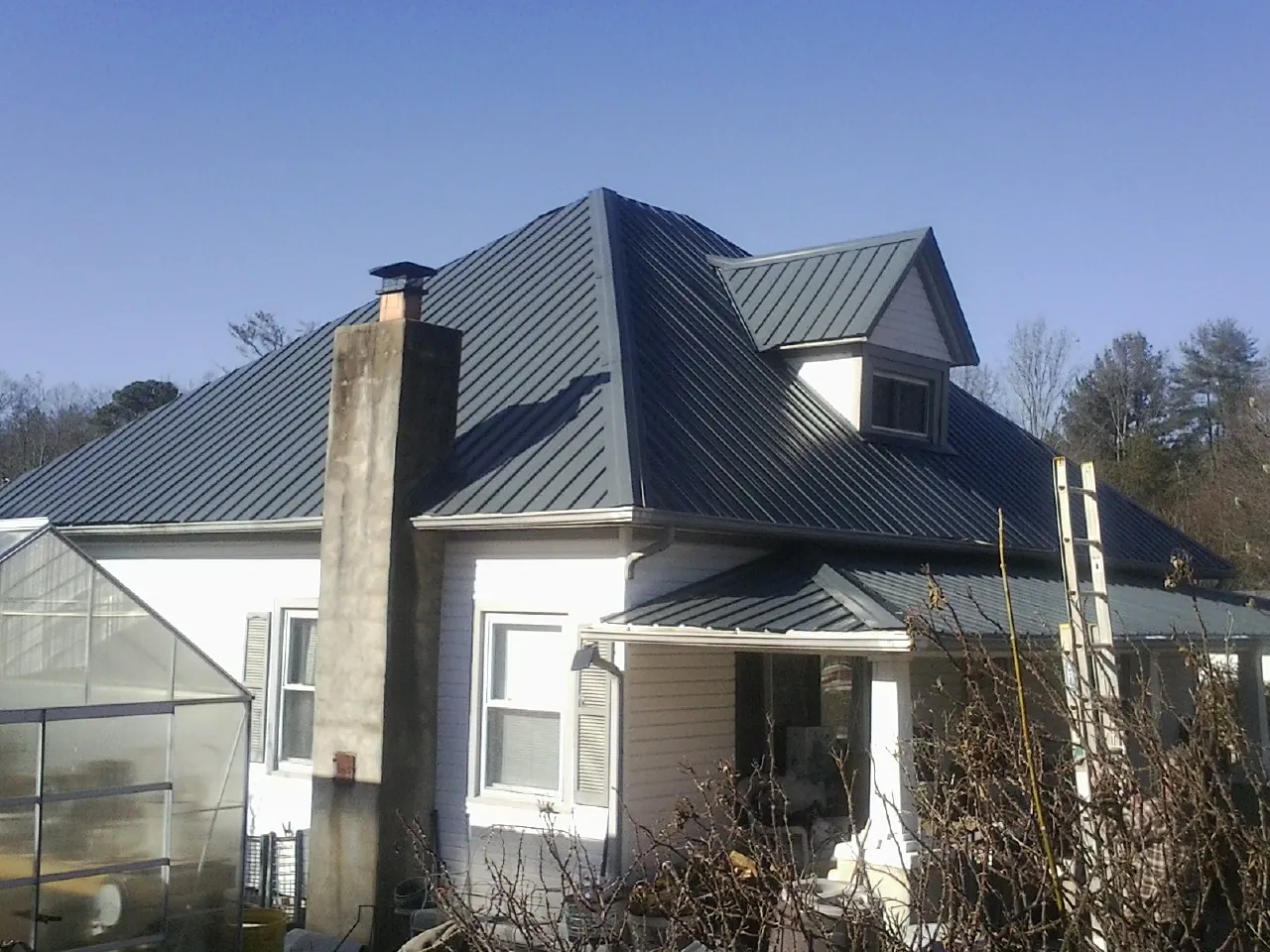 Dark blue standing seam metal roof on a white farmhouse with dormer — Slate & Tile Roof Repair by Roofing Brothers in Grand Bay