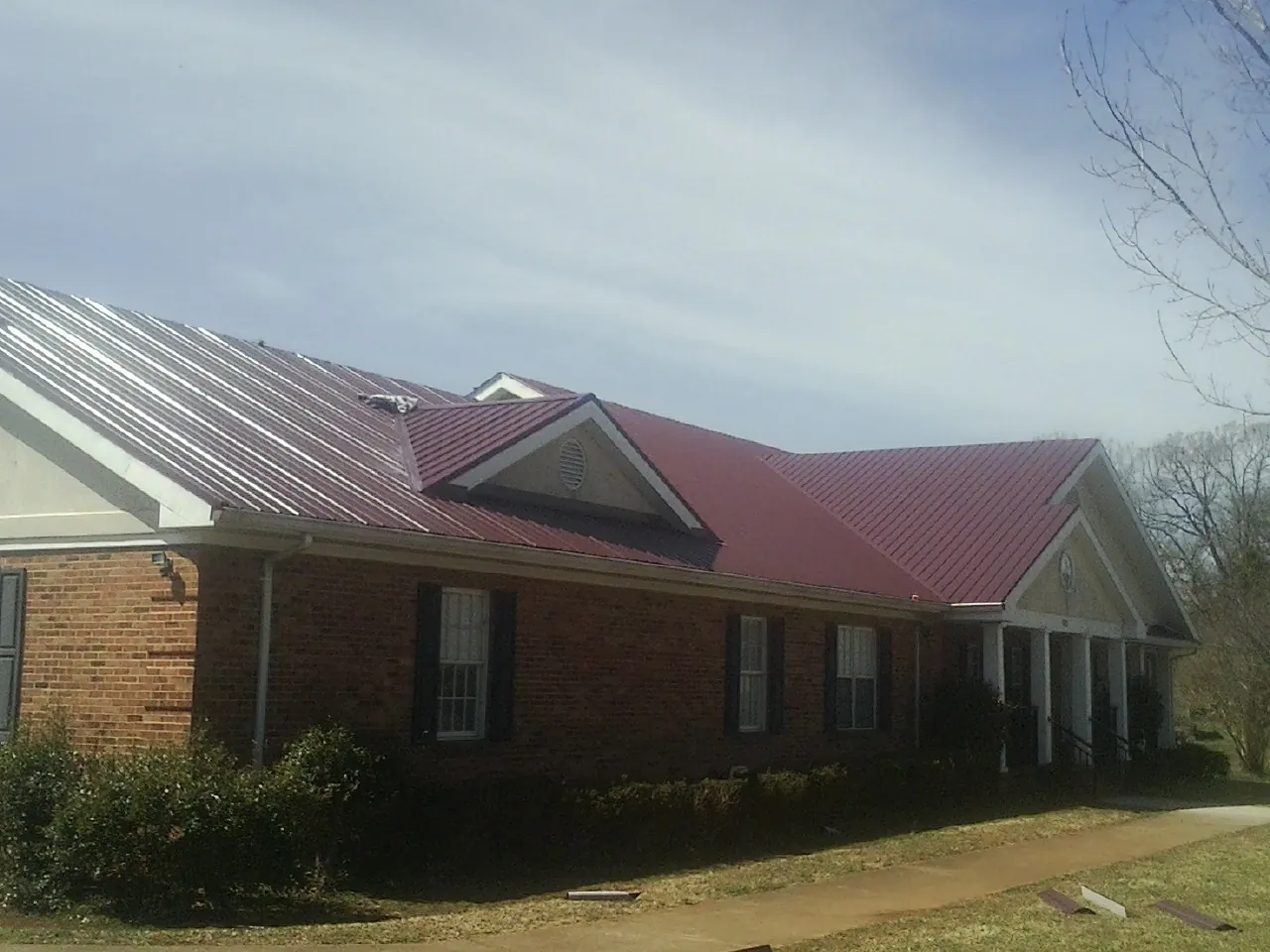 Red metal roof with gabled entries on a long brick building, from a Hail Damage Roof Repair job in Grand Bay