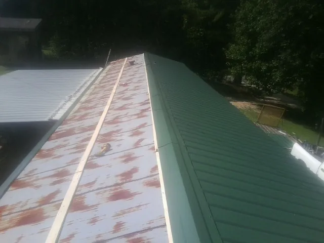 Old rusted panels beside newly installed green metal roofing — Wind Damage Roof Repair by Roofing Brothers in Grand Bay