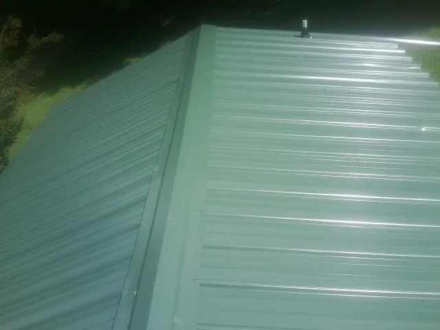 New green metal panels meeting at the ridge of a roof — Flat Roof Repair work by our crew in Grand Bay