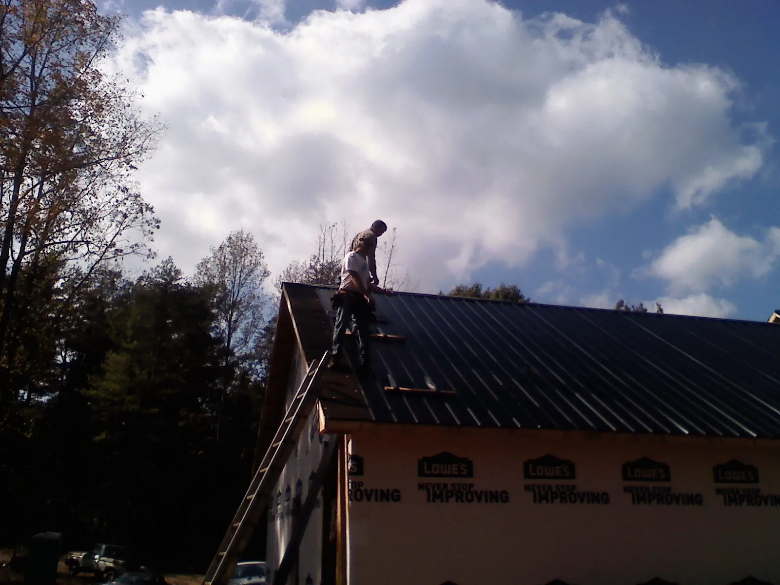 Roofer fastening dark metal panels high against a cloudy sky, from a Roof Inspection job in Grand Bay