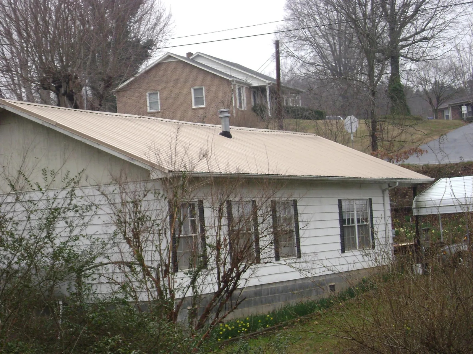 Tan metal roof on a white sided house set into a hillside — Commercial Roofing by Roofing Brothers in Grand Bay