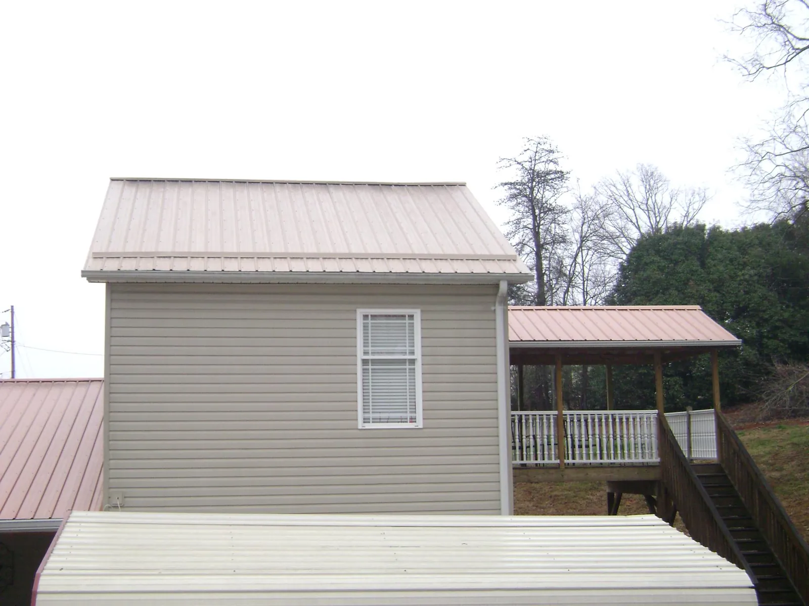 Tan metal roofs on a two story addition and attached porch, from a Roof Replacement job in Grand Bay